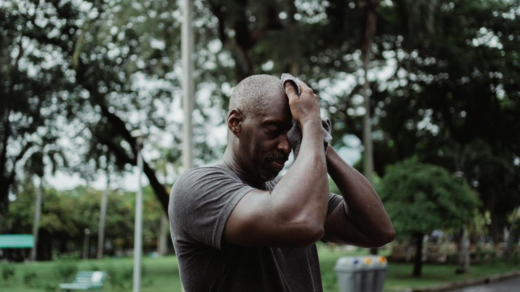 man in gray shirt with towel pressed to forehead