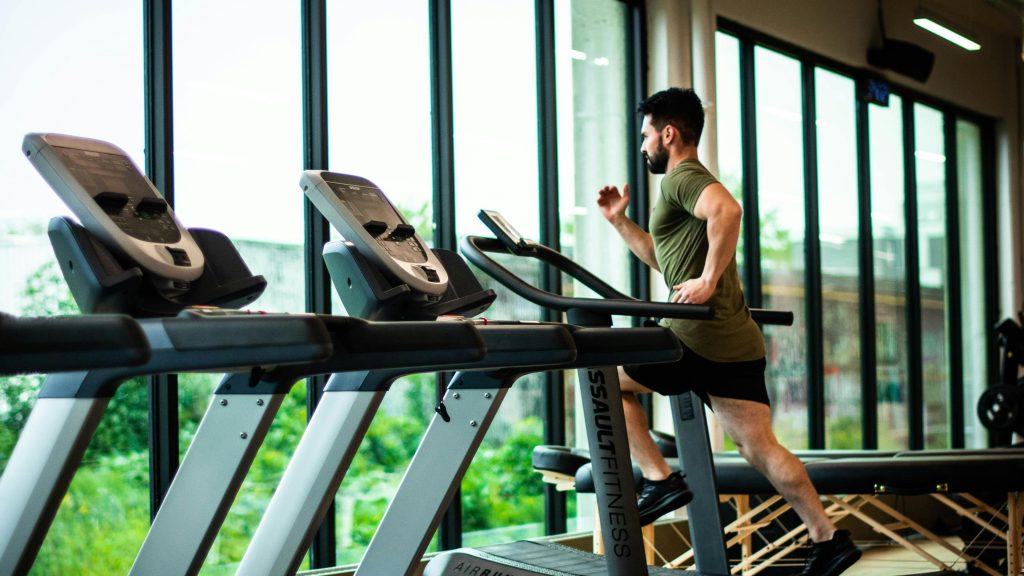 man running on treadmill in front of wall of windows