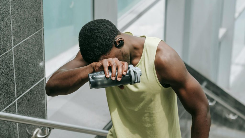 man holding water bottle with back of hand on forehead