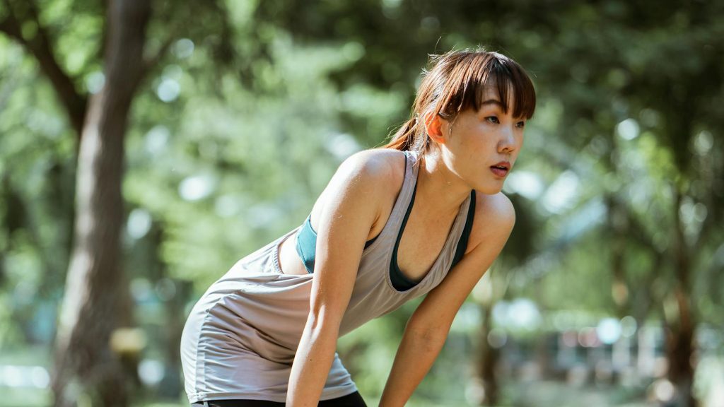 Young asian woman bent over resting after a run
