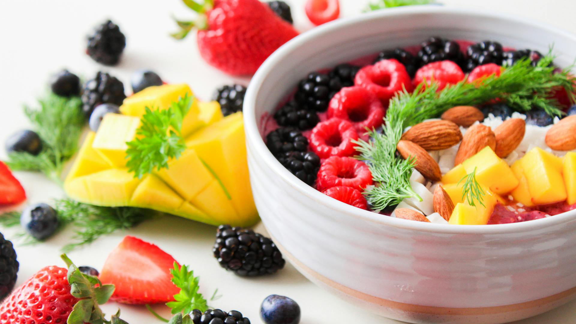 Bowl of berries and nuts surrounded by fruits and berries